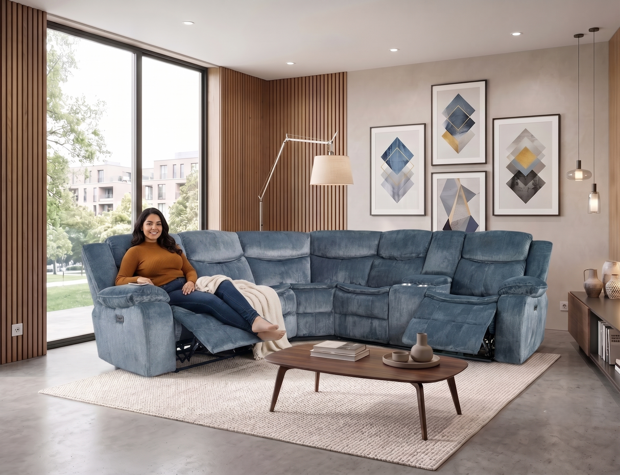 A woman relaxes in a large blue reclining sectional sofa in a modern living room. The sofa is upholstered in a textured blue fabric and includes multiple seat and back cushions.