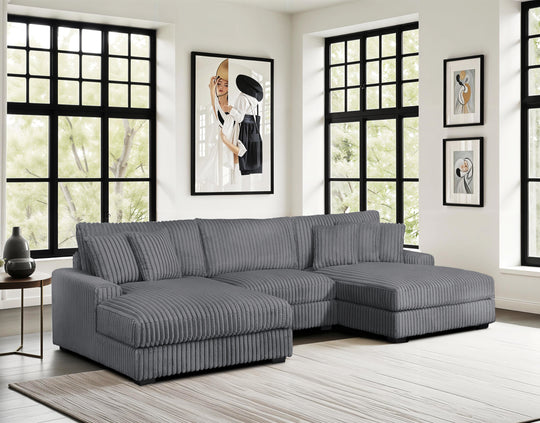 Gray sectional sofa in a living room with large windows and framed pictures on the wall.