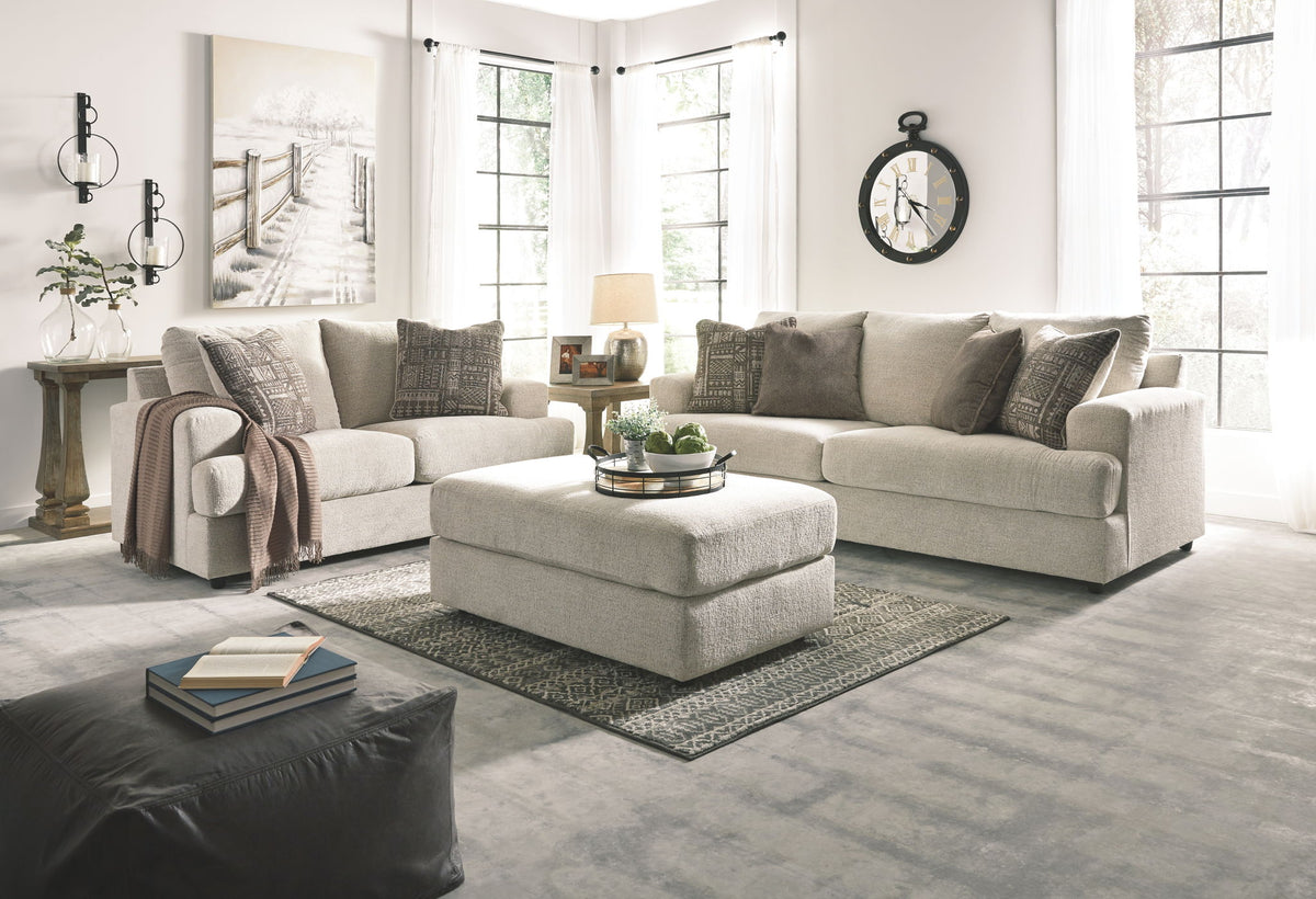 Living room with a beige sectional sofa, ottoman, and decorative items.