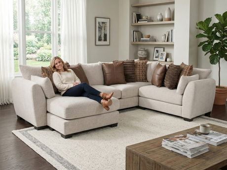 Woman sitting on a beige sectional sofa in a living room with a coffee table and decor.