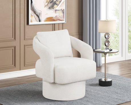 A modern barrel-style accent chair upholstered in textured off-white fabric, set in a styled living room next to a small side table with a lamp.