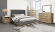 Modern bedroom with gray upholstered bed, wooden nightstand, dresser, and mirror.