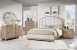 A light oak wood and upholstered bedroom furniture set in a bright, modern bedroom. The set includes a bed with a tufted headboard, a matching dresser with an arched mirror, a chest of drawers, and a nightstand.